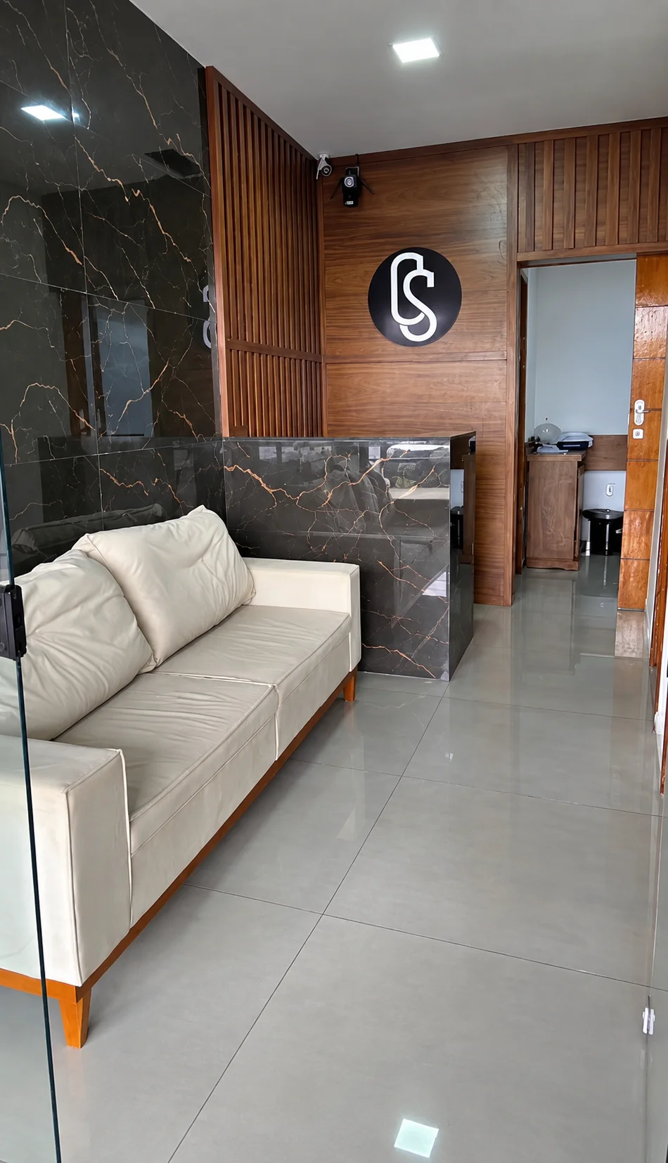 Recepção do escritório com mármore de veios cobre, painel de madeira e logo CS